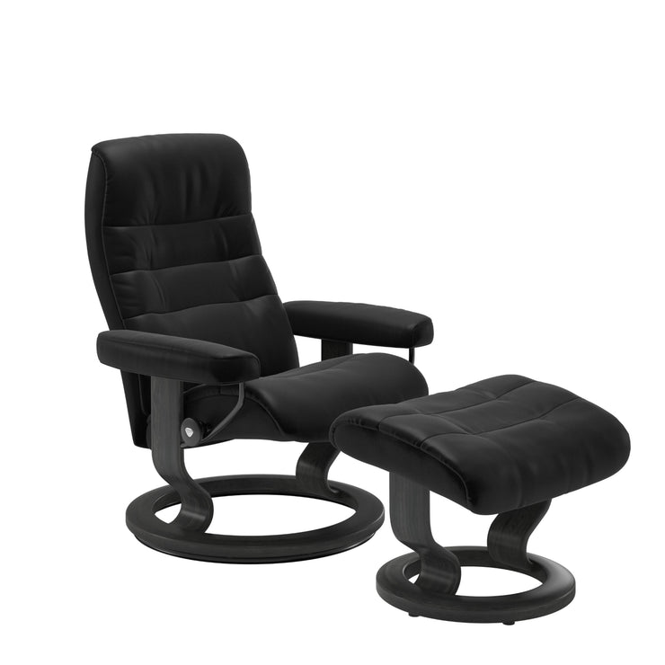 Stressless Opal M -lepotuoli ja rahi mustana: Black 19 Batick-nahkaverhoilulla ja harmaa petsatulla -Classic-puujalustalla.