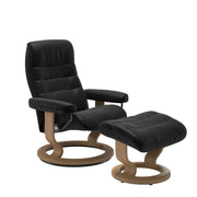 Stressless Opal M -lepotuoli ja rahi mustana: Black 19 Batick-nahkaverhoilulla ja tammi petsatulla -Classic-puujalustalla.