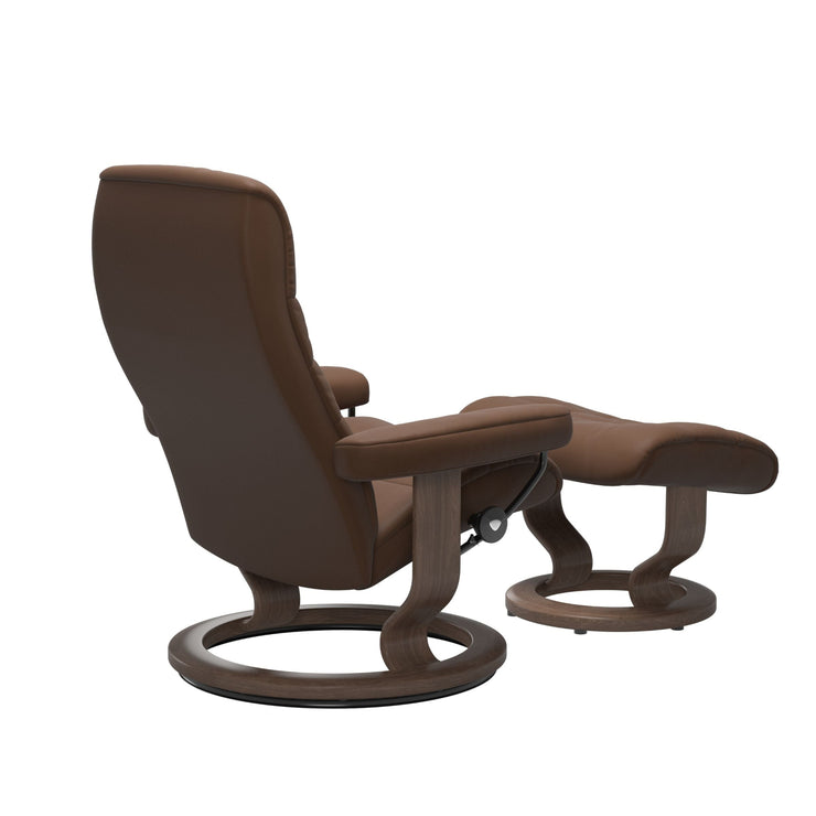 Stressless Opal M -lepotuoli ja rahi ruskeana: Warm Brown 87 Batick-nahkaverhoilulla ja Walnut 06 -Classic-puujalustalla.