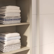 Kuvassa on mattavalkoinen Kira-liukuovikomero - toinen liukuovi avoinna ja kaappia on täydennetty näkyvissä olevilla erikseen myytävillä lisähyllyillä. Kaapin sisus on väriltään harmaata kangasjäljitelmää.