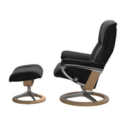 Stressless Mayfair M -lepotuoli ja rahi mustana: Black 19 Paloma-nahkaverhoilulla ja tammi petsi 04 pyökki/kiiltävä alumiini Alu 40 -Signature-yhdistelmäjalustalla.