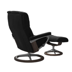 Stressless Mayfair M -lepotuoli ja rahi mustana: Black 19 Paloma-nahkaverhoilulla ja wenge petsattu pyökki 11/kiiltävä alumiini Alu40 -Signature-yhdistelmäjalustalla.