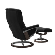 Stressless Mayfair M -lepotuoli ja rahi mustana: Black 19 Paloma-nahkaverhoilulla ja wenge petsattu pyökki 11/kiiltävä alumiini Alu40 -Signature-yhdistelmäjalustalla.