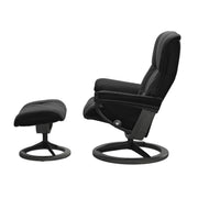 Stressless Mayfair M -lepotuoli ja rahi mustana: Black 19 Paloma-nahkaverhoilulla ja harmaa petsattu pyökki 08/mattamusta 45 metalli -Signature-yhdistelmäjalustalla.