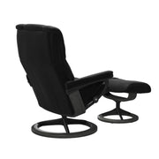 Stressless Mayfair M -lepotuoli ja rahi mustana: Black 19 Paloma-nahkaverhoilulla ja harmaa petsattu pyökki 08/mattamusta 45 metalli -Signature-yhdistelmäjalustalla.