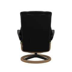 Stressless Mayfair M -lepotuoli ja rahi mustana: Black 19 Paloma-nahkaverhoilulla ja tammi petsi 04/mattamusta 45 metalli -Signature-yhdistelmäjalustalla.