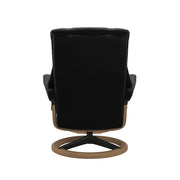 Stressless Mayfair M -lepotuoli ja rahi mustana: Black 19 Paloma-nahkaverhoilulla ja tammi petsi 04/mattamusta 45 metalli -Signature-yhdistelmäjalustalla.