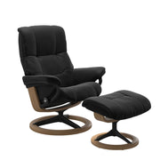Stressless Mayfair M -lepotuoli ja rahi mustana: Black 19 Paloma-nahkaverhoilulla ja tammi petsi 04/mattamusta 45 metalli -Signature-yhdistelmäjalustalla.