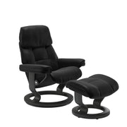 Stressless Ruby M -lepotuoli ja rahi mustana: Black 19 Batick-nahkaverhoilulla ja harmaa petsatulla -Classic-puujalustalla.