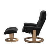 Stressless Ruby M -lepotuoli ja rahi mustana: Black 19 Batick-nahkaverhoilulla ja tammi petsatulla -Classic-puujalustalla.