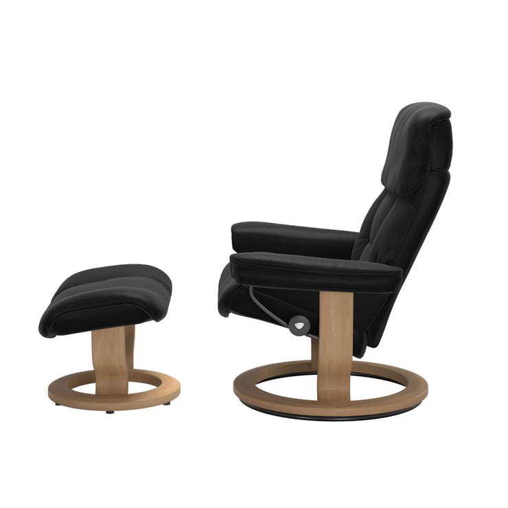 Stressless Ruby M -lepotuoli ja rahi mustana: Black 19 Batick-nahkaverhoilulla ja tammi petsatulla -Classic-puujalustalla.