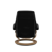 Stressless Ruby M -lepotuoli ja rahi mustana: Black 19 Batick-nahkaverhoilulla ja tammi petsatulla -Classic-puujalustalla.