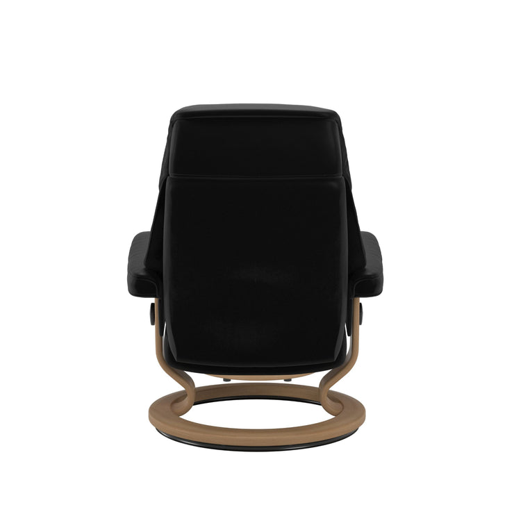 Stressless Ruby M -lepotuoli ja rahi mustana: Black 19 Batick-nahkaverhoilulla ja tammi petsatulla -Classic-puujalustalla.