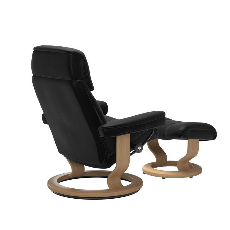 Stressless Ruby M -lepotuoli ja rahi mustana: Black 19 Batick-nahkaverhoilulla ja tammi petsatulla -Classic-puujalustalla.