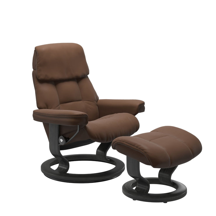 Stressless Ruby M -lepotuoli ja rahi ruskeana: Warm Brown 87 Batick-nahkaverhoilulla ja harmaa petsatulla -Classic-puujalustalla.