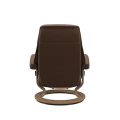 Stressless Ruby M -lepotuoli ja rahi ruskeana: Warm Brown 87 Batick-nahkaverhoilulla ja tammi petsatulla -Classic-puujalustalla.