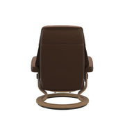 Stressless Ruby M -lepotuoli ja rahi ruskeana: Warm Brown 87 Batick-nahkaverhoilulla ja tammi petsatulla -Classic-puujalustalla.