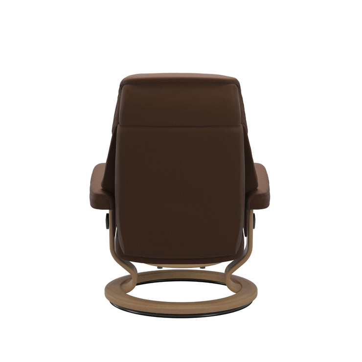 Stressless Ruby M -lepotuoli ja rahi ruskeana: Warm Brown 87 Batick-nahkaverhoilulla ja tammi petsatulla -Classic-puujalustalla.