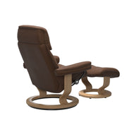 Stressless Ruby M -lepotuoli ja rahi ruskeana: Warm Brown 87 Batick-nahkaverhoilulla ja tammi petsatulla -Classic-puujalustalla.