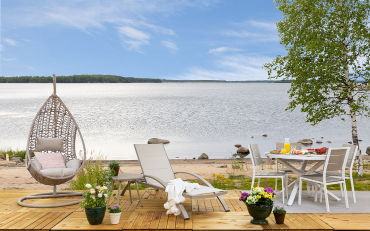 Kuvassa on beige Suvi-riippukeinu Suvi-sohvapöydän, Suvi Textiline -aurinkotuolin ja pyöreän Suvi Aintwood-ruokaryhmän kanssa. Kuvassa lisäksi Mattokympin pellavanvärinen Pilke-matto ja valkoinen Sävel Tupsu -torkkupeitto, sekä Kesälahti koristetyyny.