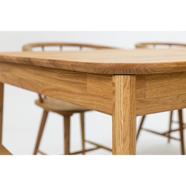 Lähikuvassa on luonnonvärisen Vera-tammipöydän pyöristettykulmaista rakennetta kuvattuna erikseen myytävien Aida-tammituolien kanssa.