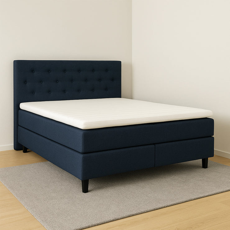 Sininen Hilding Feel -jenkkisänky hiilenmustilla 14 cm korkeilla Royal -tammijaloilla ja yhtenäisellä Hilding Hybrix Air Coolmax -sijauspatjalla. Kuvan Feel -sängynpääty myydään erikseen. Stailattu visualisointi.