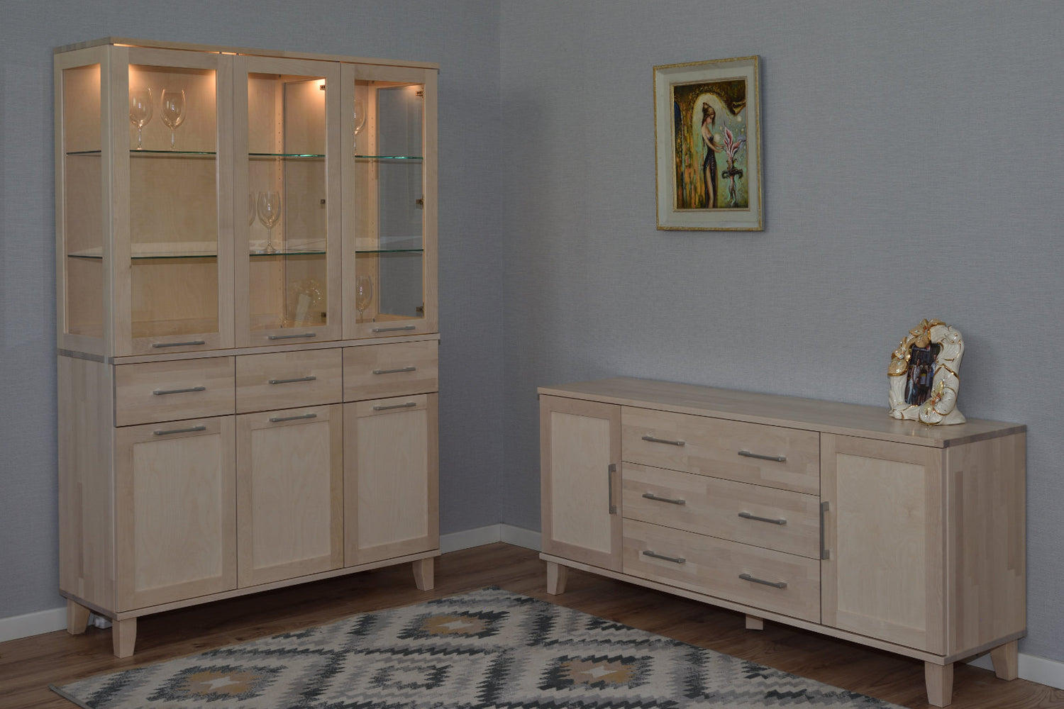 Kuvassa on valkolakattu Vuokatti-vitriini. Vitriinissä on lasikaapisto lasihyllyillä, alaosan tilava senkki kaappien peiliovilla, sekä pitkänmalliset RST-vetimet. Lasikaapin sisällä olevat valot/viinilasit eivät kuulu senkin hintaan. Kuvassa on lisäksi Vuokatti-sarjan senkki 24/1.