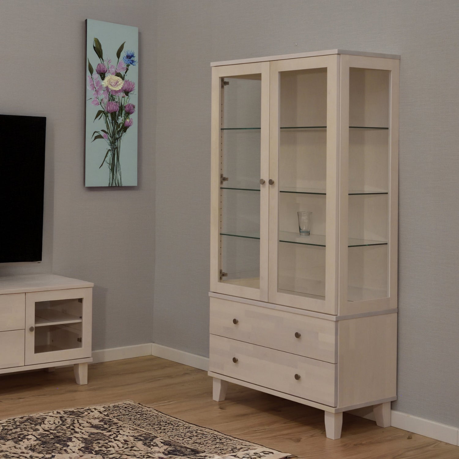 Kuvassa on valkolakattu Vuokatti-vitriini. Vitriinissä on lasikaappi lasihyllyillä, alaosan isot laatikot, sekä nikkelinväriset D26-nuppivetimet.