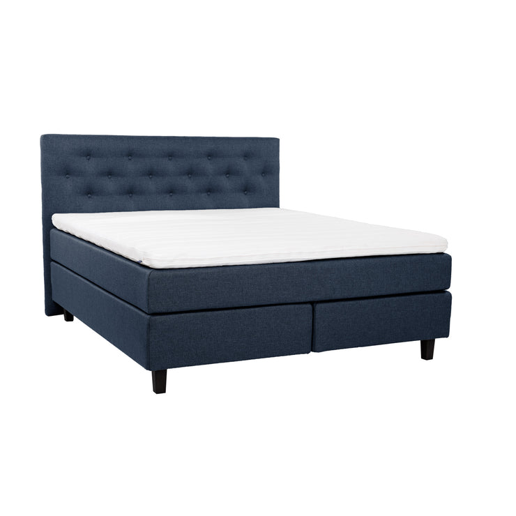 Sininen Hilding Feel -jenkkisänky 160 x 200 cm hiilenmustilla 14 cm korkeilla Royal -tammijaloilla ja yhtenäisellä Hilding Hybrix Air Coolmax -sijauspatjalla. Kuvan Feel -sängynpääty myydään erikseen.