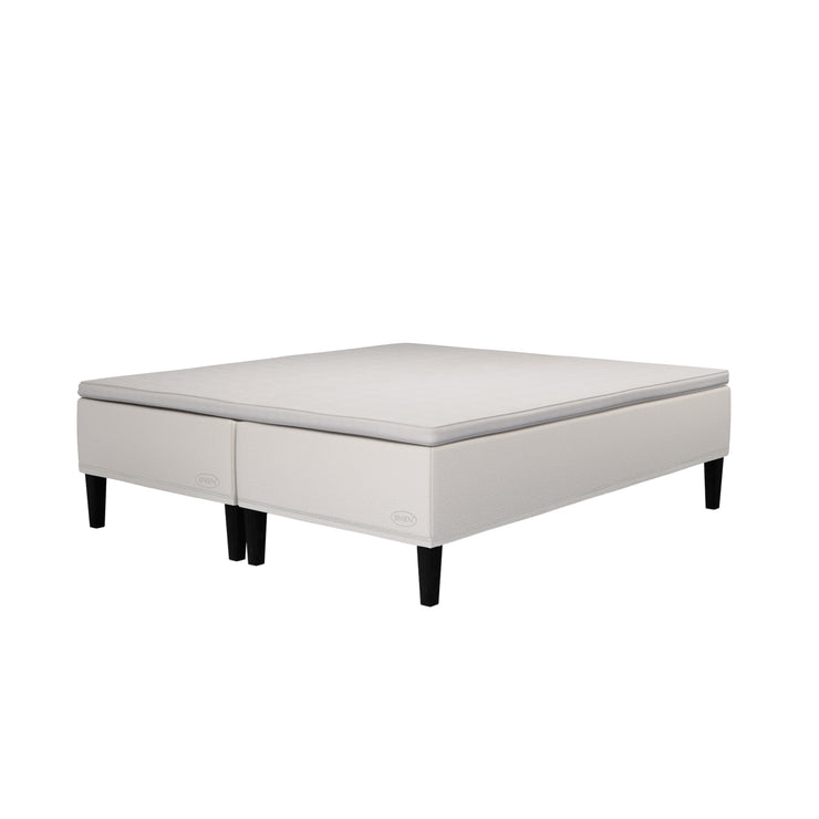 Jensen Carat -runkopatjasängyn beige verhoiluväri ja nelikulmaiset 23 cm korkeat mustat tammijalat. Yhtenäinen TempSmart -sijauspatja ja jalat sisältyvät hintaan.
