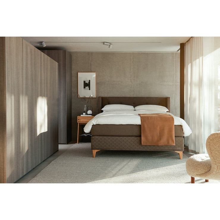 Jensen Majestic -jenkkisänky on Nest-sängynpäädyn kanssa sisustuksellinen kokonaisuus, kuvassa on ruskea verhoiluväri ja Eicon-tammijalat. Jensenin sängynpääty ja tamminen Eicon-yöpöytä myydään erikseen.