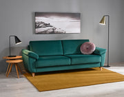 Monika 3-istuttava sohva petroolin värisellä kangasverhoilulla ja puujaloilla.