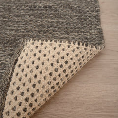 Lähikuvassa tummanharmaan Oona-villamaton sileä ja tiivis pinta, sekä maton pohjapuoli.