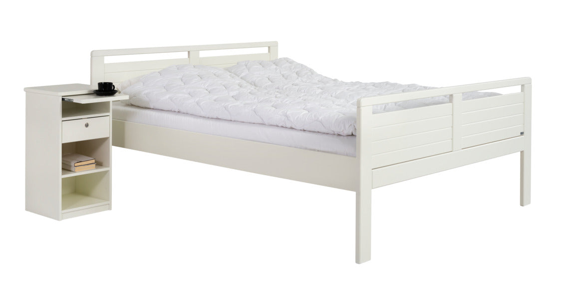 Seniori-sarjan yöpöytä vetotasolla tuo lisää laskutilaa makuuhuoneeseen. Kuvassa myös maalattu valkoinen Seniori-sänky.