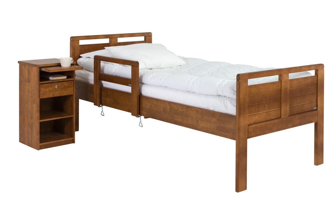 Seniori-sarjan yöpöytä vetotasolla tuo lisää laskutilaa makuuhuoneeseen. Kuvassa myös Seniori-sänky värissä petsattu pähkinä.